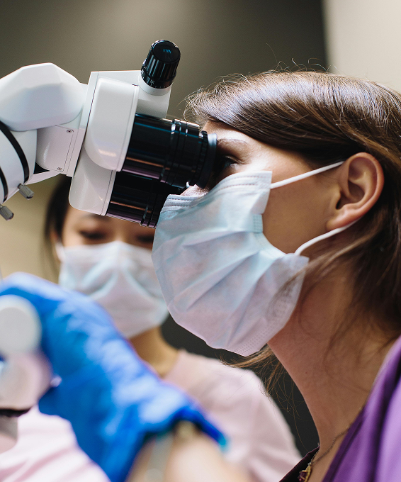 Clinician in a surgical mask using a microscope during an elective medical procedure